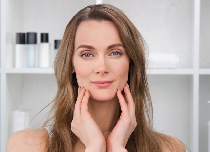 prikaz devojke koja se drži za svoje lice, iza nje proizvodi namenjeni licu