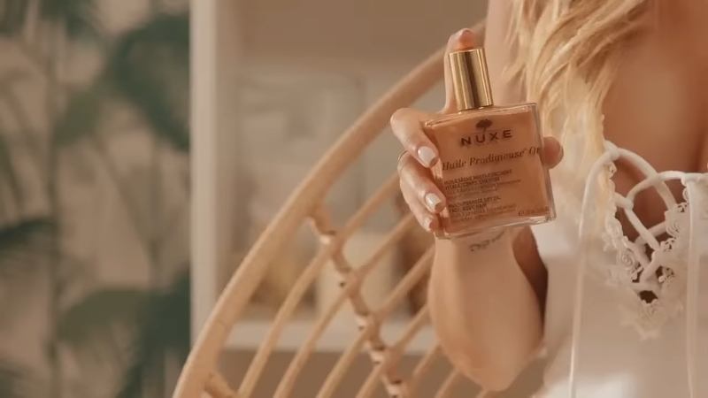 Žena u svetloj haljini drži bočicu Nuxe Huile Prodigieuse Or ulja