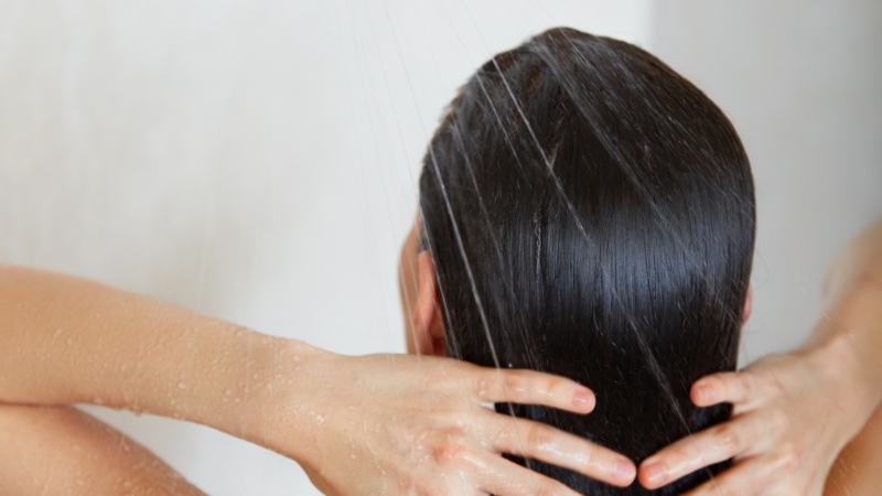 Žena pod tušem pere kosu