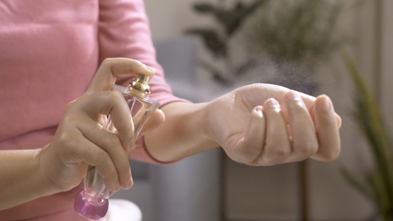 Žena nanosi parfem na unutrašnju stranu ručnog zgloba iz male staklene bočice