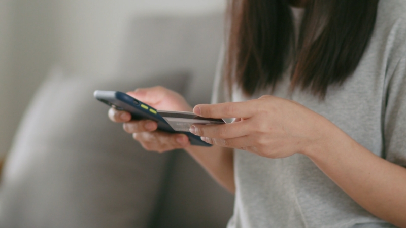 Žena prilikom online kupovine drži u jednoj ruci telefon, a u drugoj kreditnu karticu