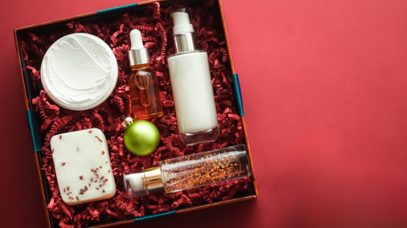 Otvorena poklon kutija sa kremom, serumom, losionom i sapunom na crvenoj podlozi