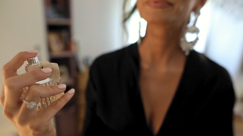 Žena u crnoj haljini drži bočicu parfema u ruci