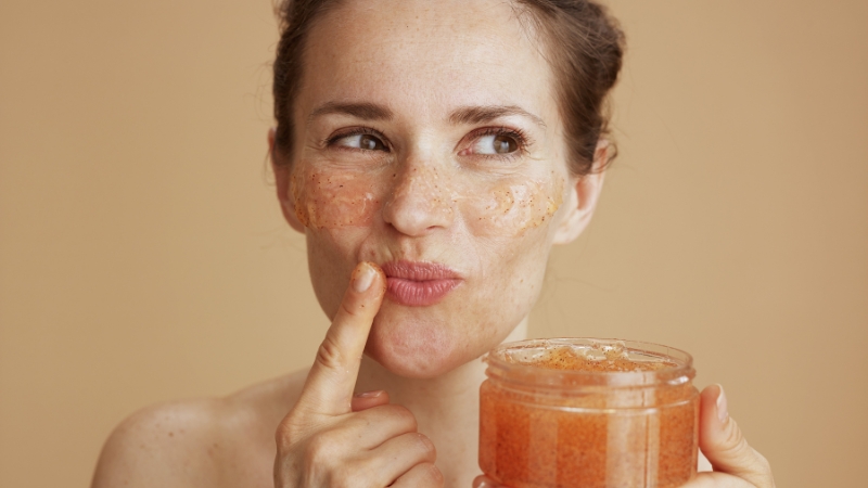 Žena sa nanetim pilingom na licu drži teglicu proizvoda